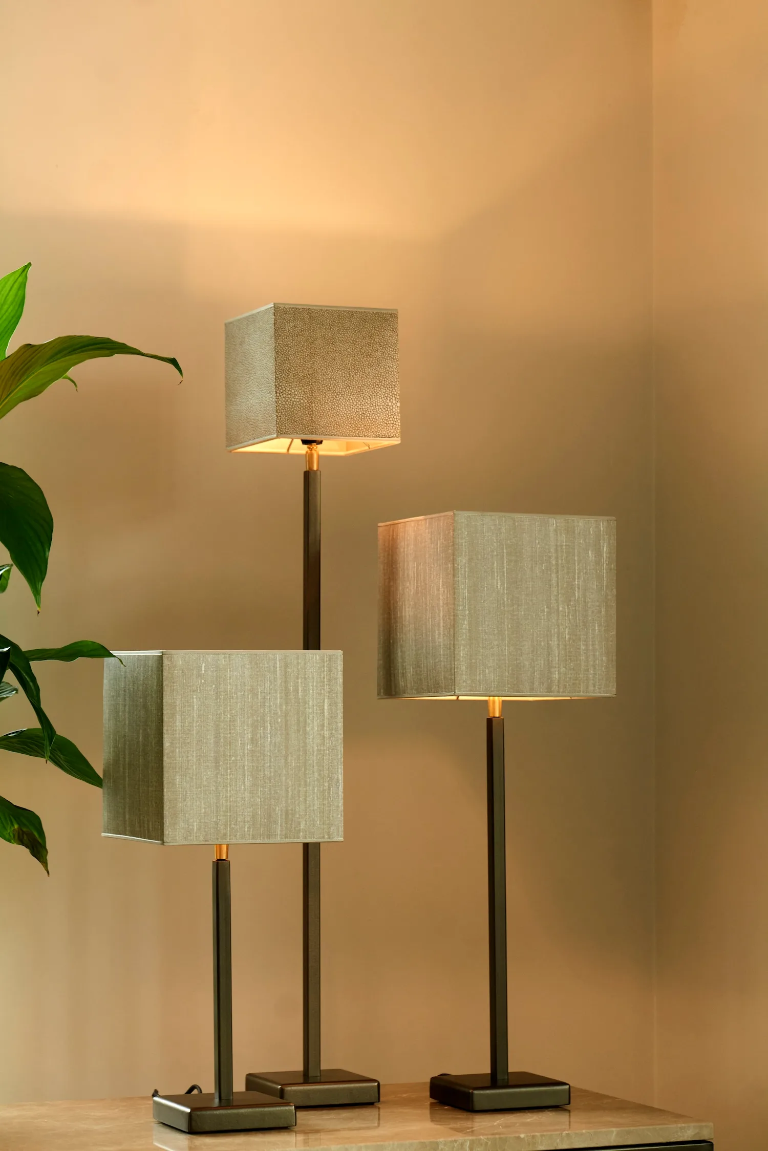 Three table lamps of varying heights with beige square shades and dark metal bases, styled in a cozy interior.