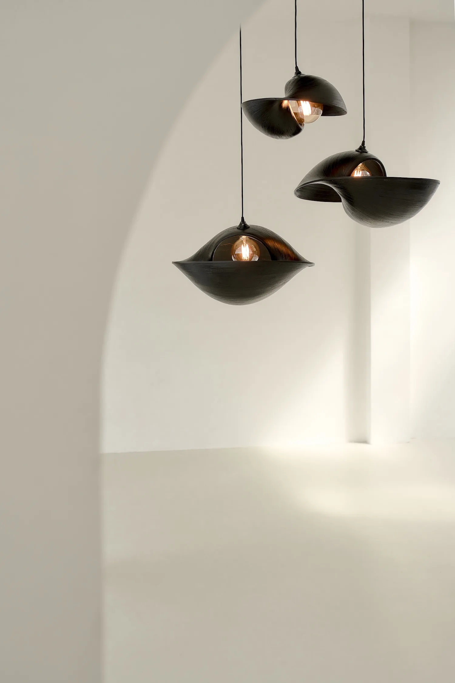 Set of three dark wood Valbonne ceiling lights in a clean, white space with soft lighting.