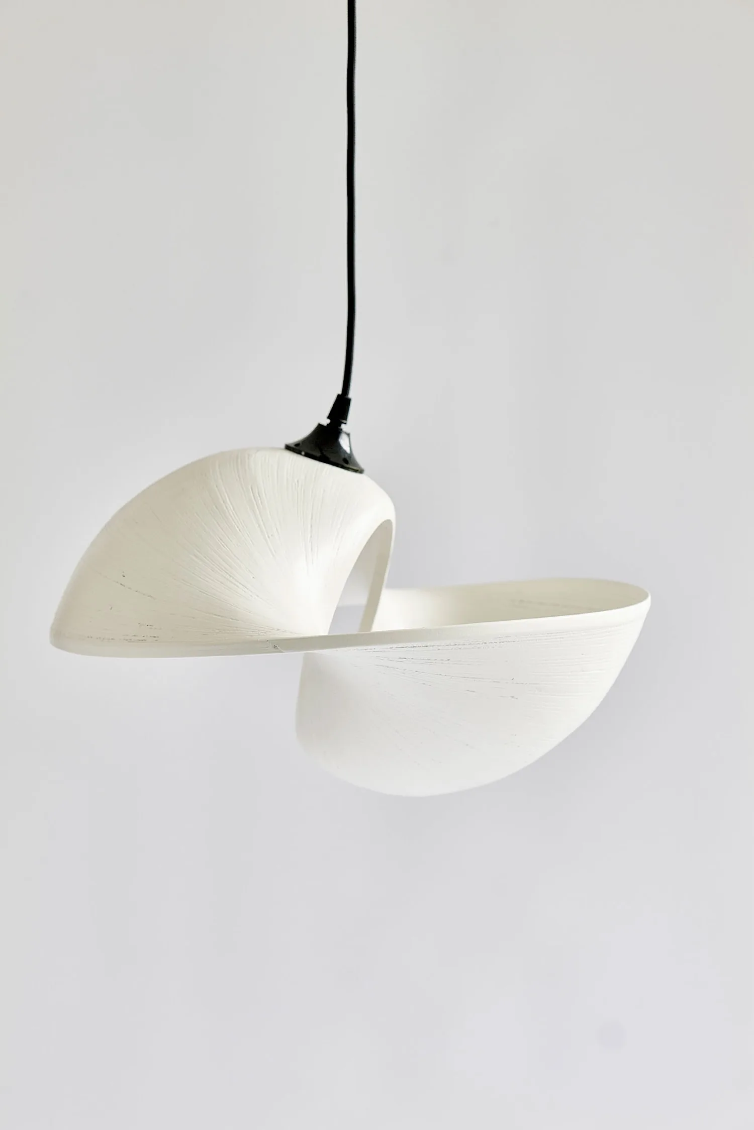 White Valbonne Air ceiling light with sculptural, fluid shape hanging in front of a plain background.