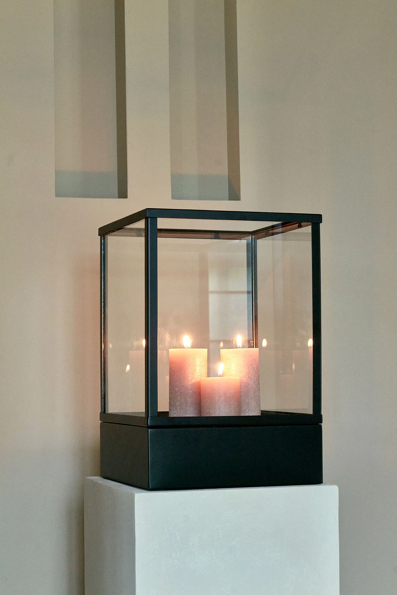 Velas hurricane lantern with a black frame and glass walls, holding three softly glowing pillar candles.