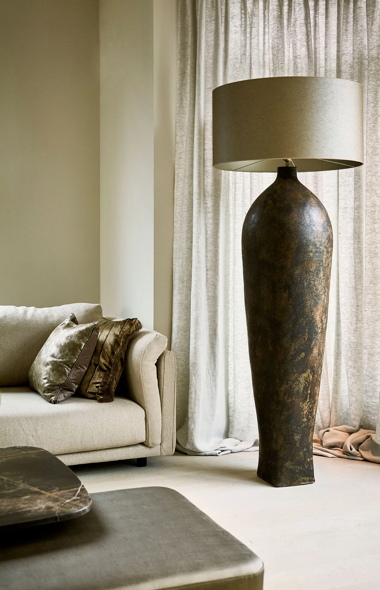Vorera Vase floor lamp with a large, sculptural ceramic base and wide beige shade beside a neutral-toned sofa.