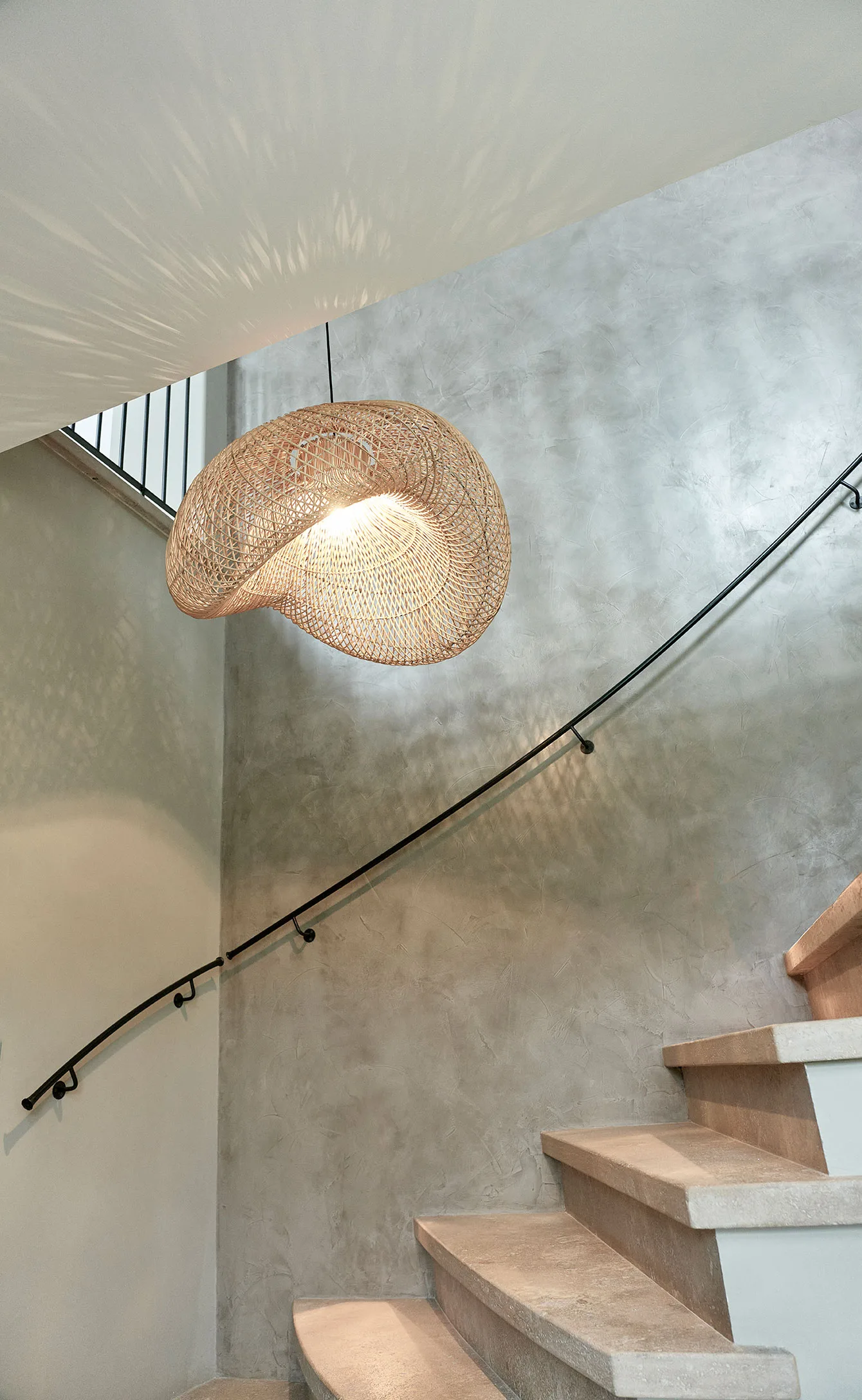Bamboo basket pendant light casting shadows on ceiling and walls of a modern concrete stairwell.
