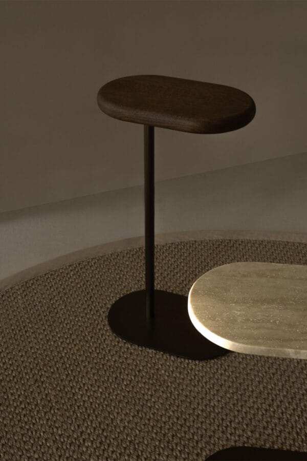 Close-up of the Axel Butler table with a dark wood top and black metal base, placed on a woven rug.