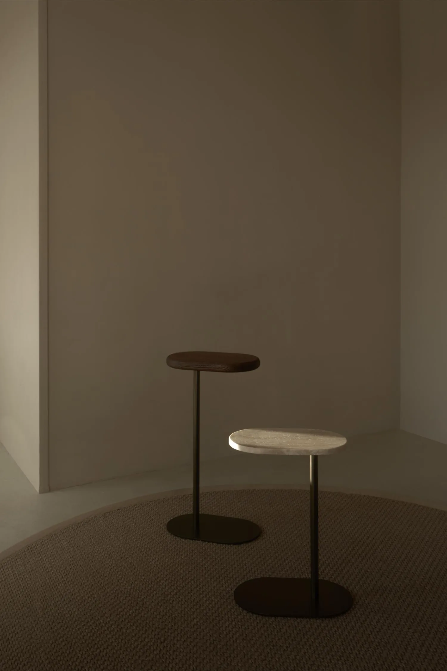Axel Butler tables in two finishes—wood and travertine—set in a softly lit minimalist space.