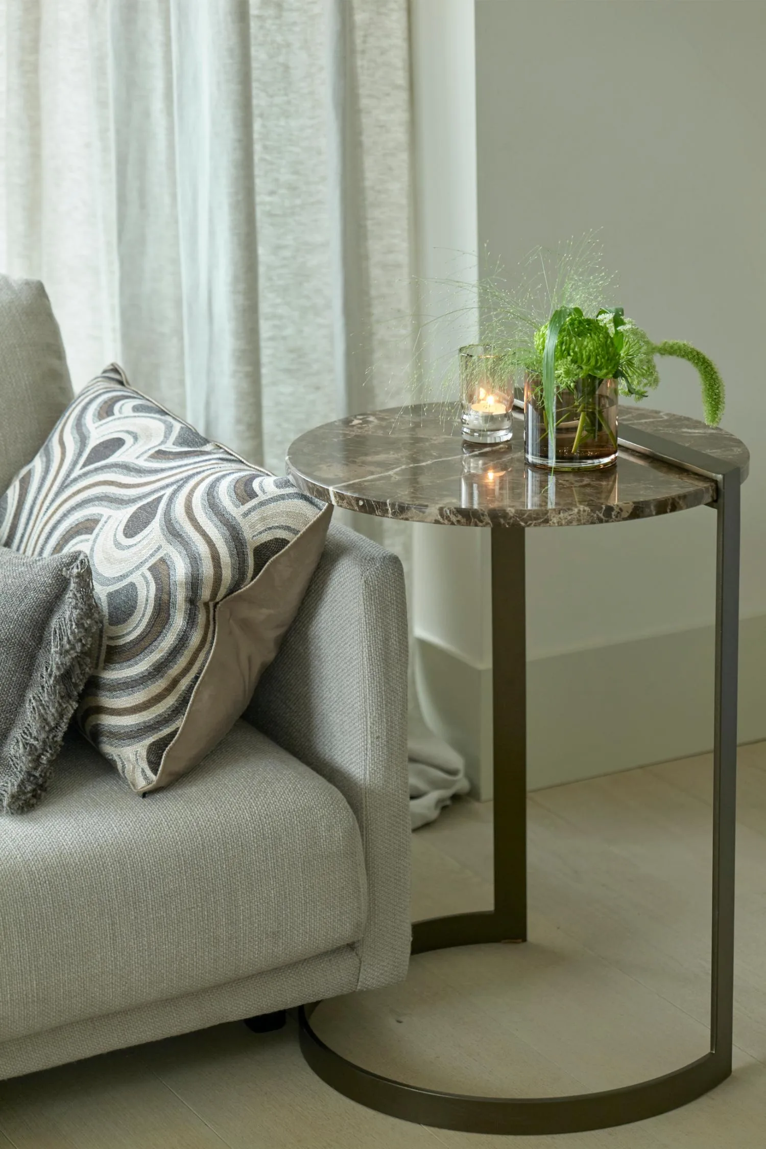 Butler side table with a marble top styled next to a grey sofa, holding a candle and green floral arrangement.