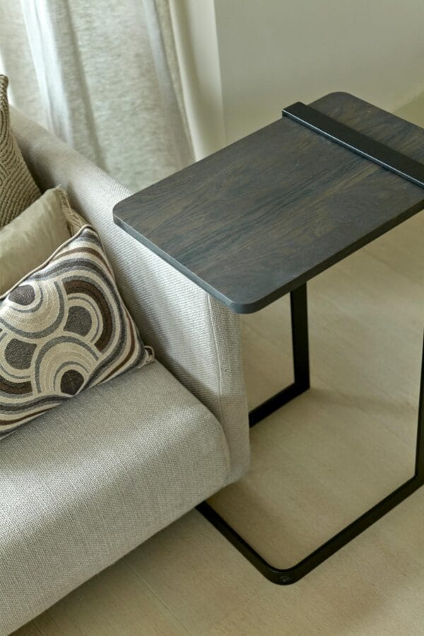 Butler side table with a rectangular dark wood top and black metal base positioned beside a light grey sofa.