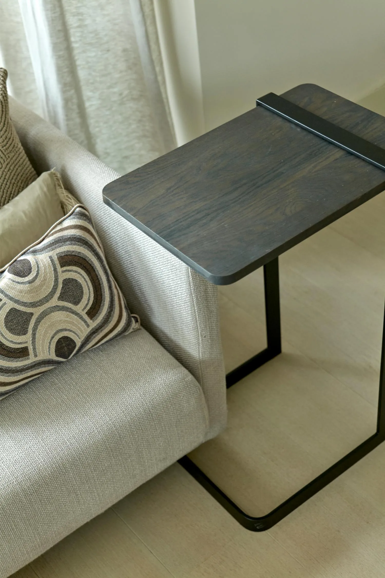 Butler side table with a rectangular dark wood top and black metal base positioned beside a light grey sofa.