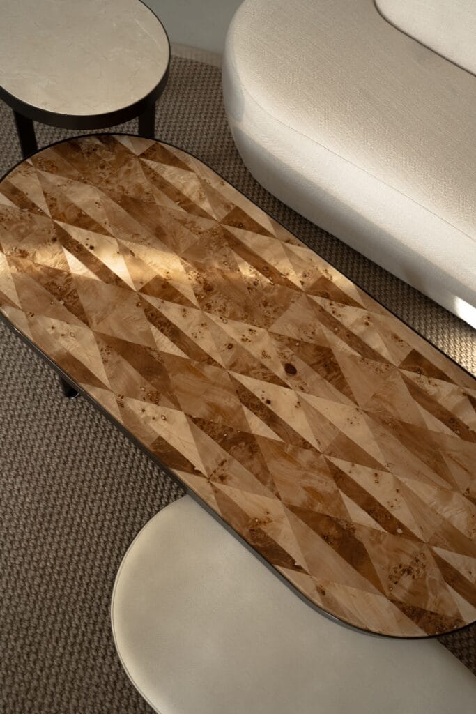 Coffee table with a patterned wood veneer top beside a light sofa and round marble table.
