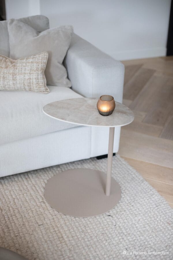 Como Butler side table with a light stone top and round metal base, styled beside a light grey sofa with a lit candle on top.