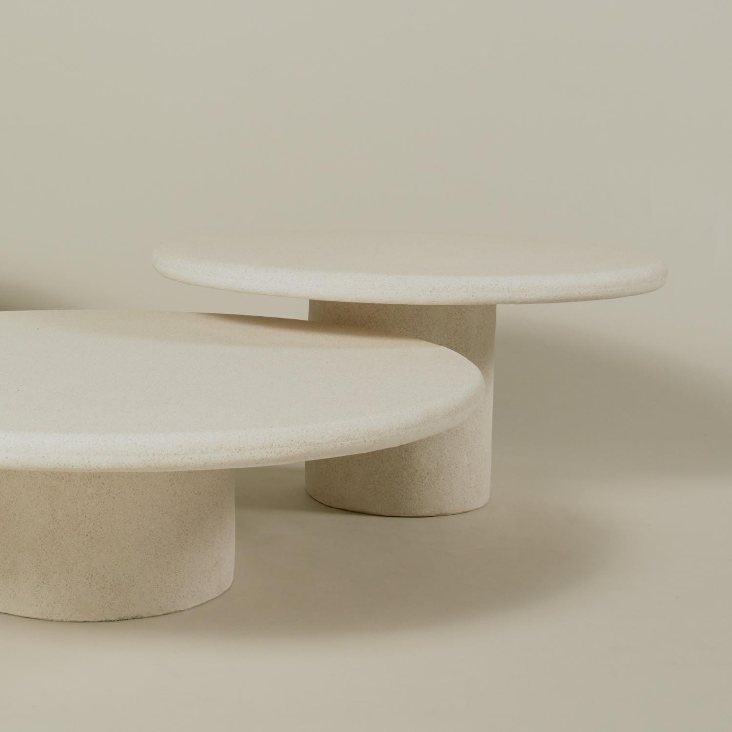 Minimalist set of two round, off-white stone coffee tables with cylindrical bases, styled against a neutral beige backdrop.