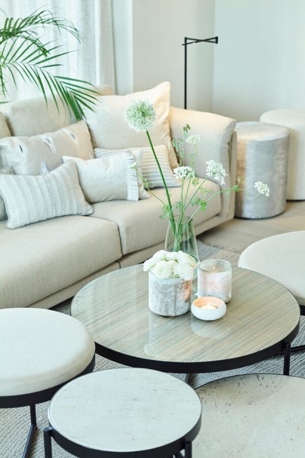 Round Lucca coffee tables with soft neutral tops and glass finishes styled with candles and fresh white flowers in a bright living room.
