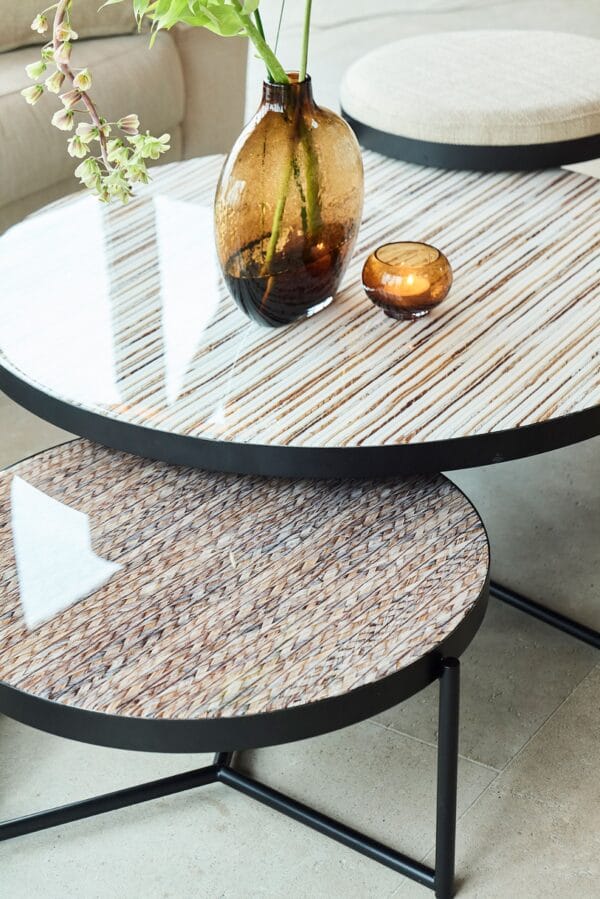 Close-up of Lucca tables with glossy, striped glass tops and black metal bases, styled with amber glass vases.