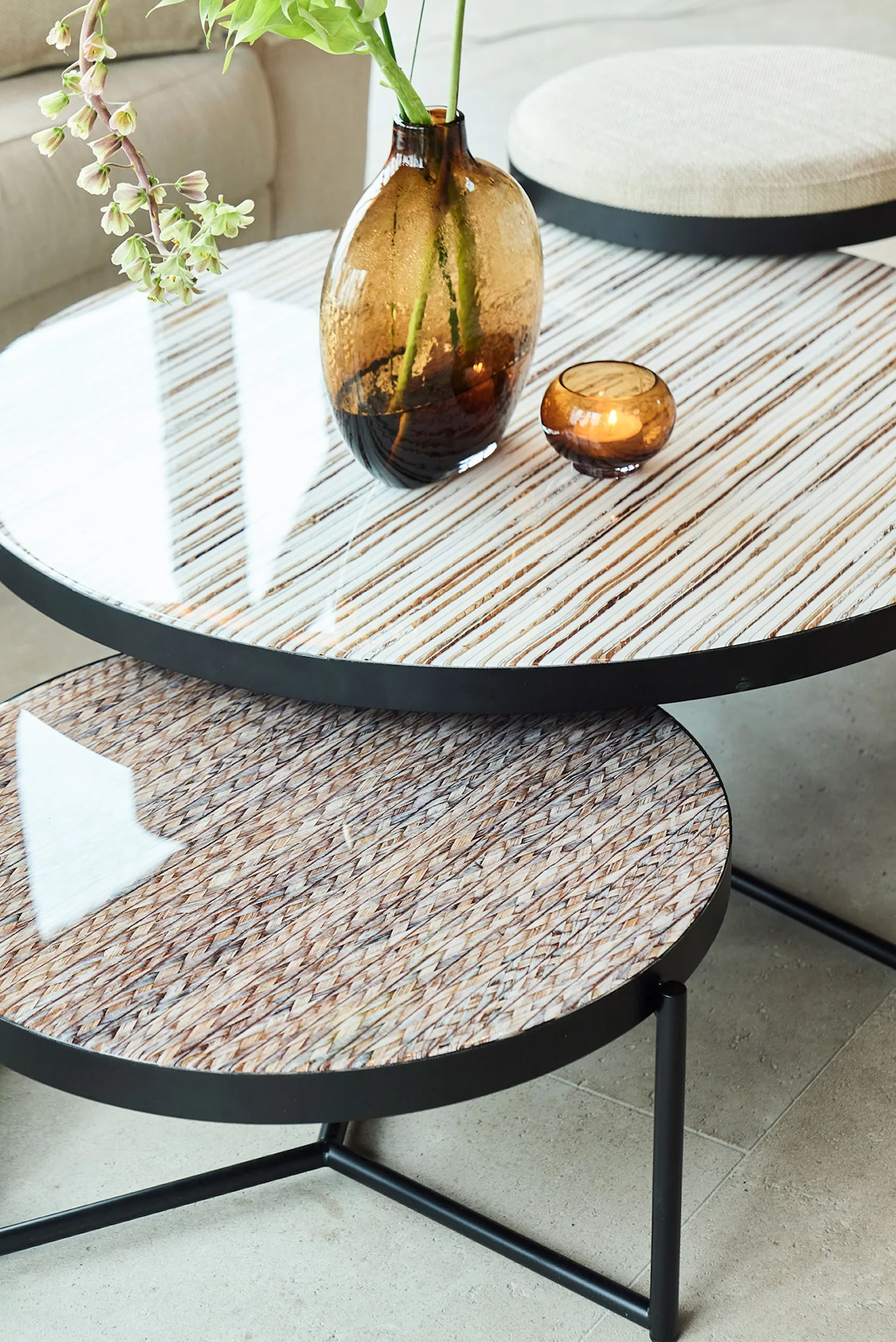 Close-up of Lucca tables with glossy, striped glass tops and black metal bases, styled with amber glass vases.