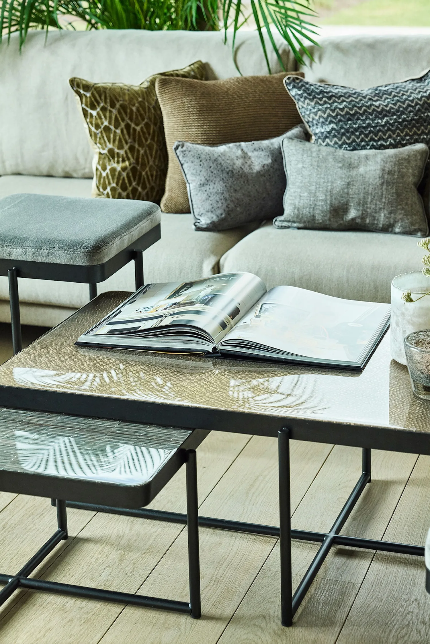 Lucca tables in various textured glass finishes, with an open magazine and grey velvet pouf in a cozy living room.