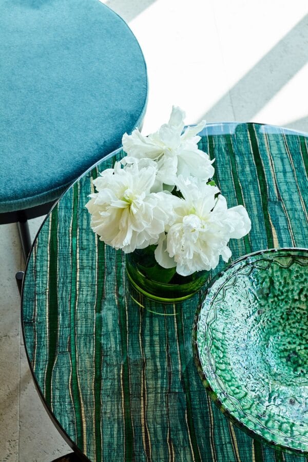 Round Lucca table with vibrant green patterned glass top, styled with white flowers and a green ceramic bowl.