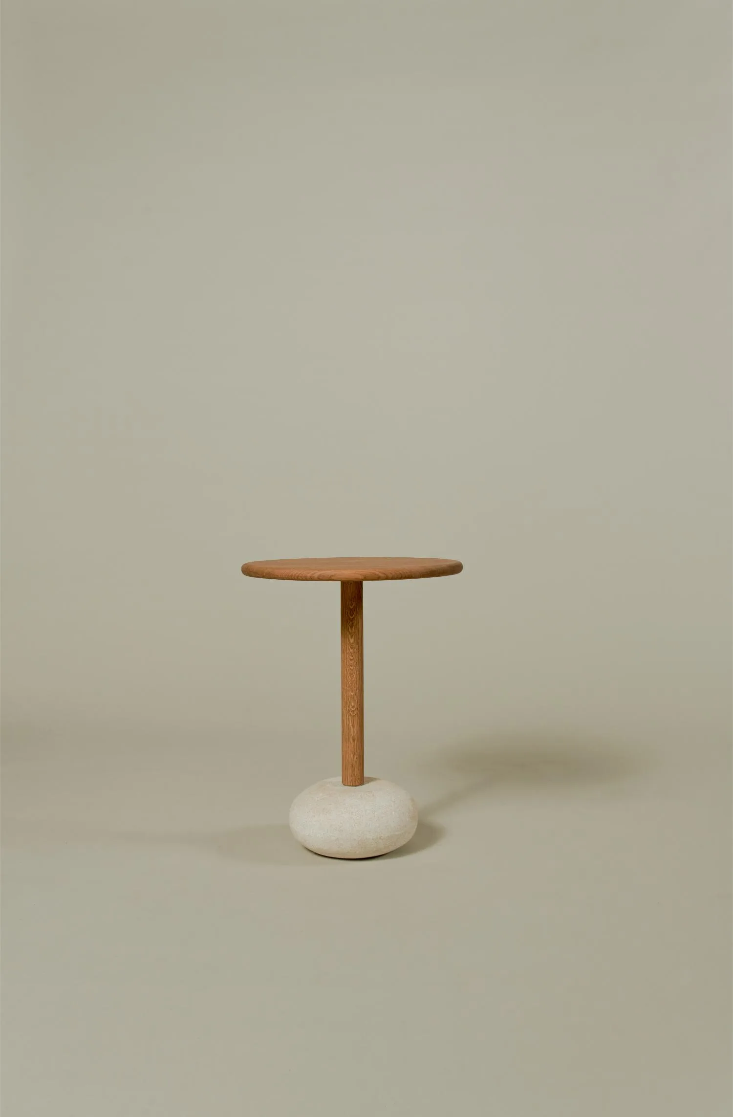 Minimalist studio view of the Owen side table featuring a round oak top and sculptural pebble-shaped base.