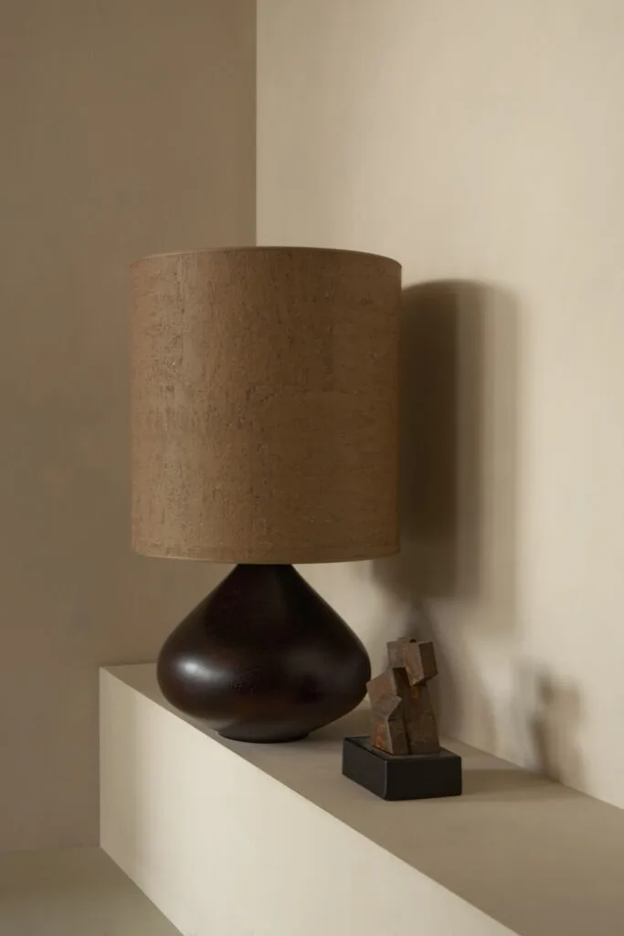 Dark sculptural table lamp with a textured cylindrical shade next to a small abstract sculpture.