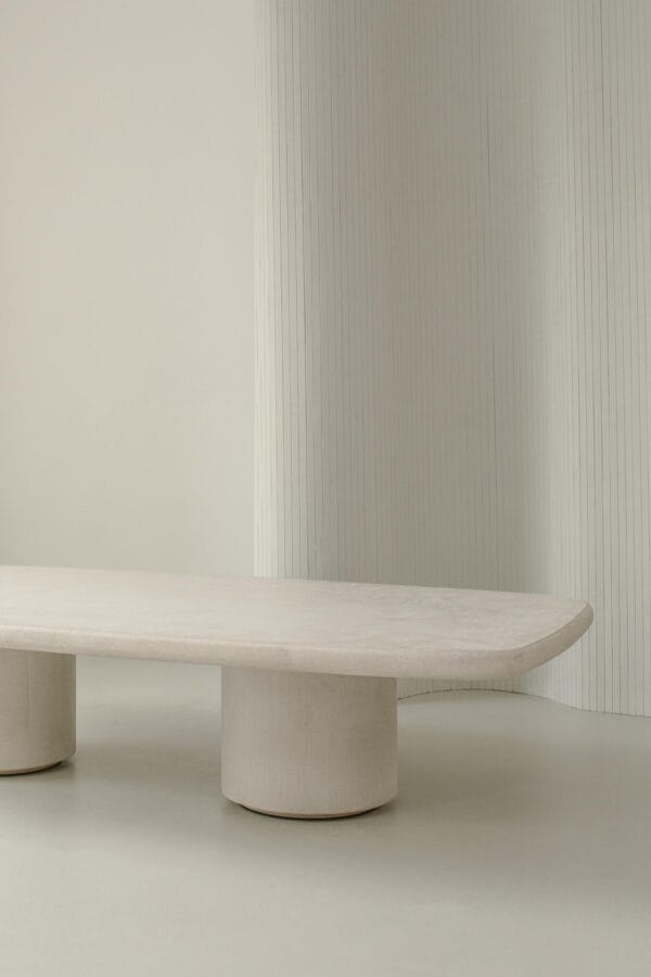 Close-up of the Venice coffee table in stucco with rounded edges and cylindrical legs, set against a minimal backdrop.