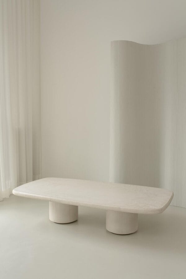 Venice coffee table in stucco finish placed in a soft-toned room with sheer curtains and a sculptural divider.