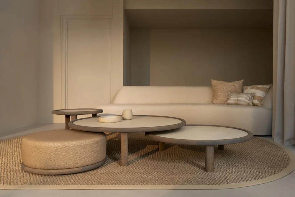 Amalfi Coffee Table Set with layered round tables and matching pouf, in front of a curved sofa in a neutral interior.