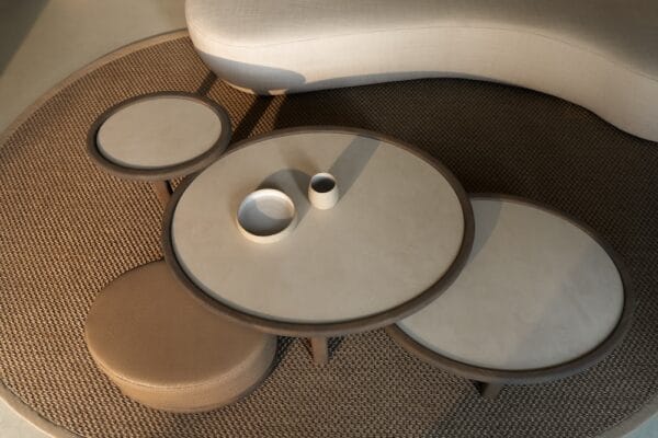 Amalfi Coffee Table Set with layered round tables and matching pouf, in front of a curved sofa in a neutral interior.