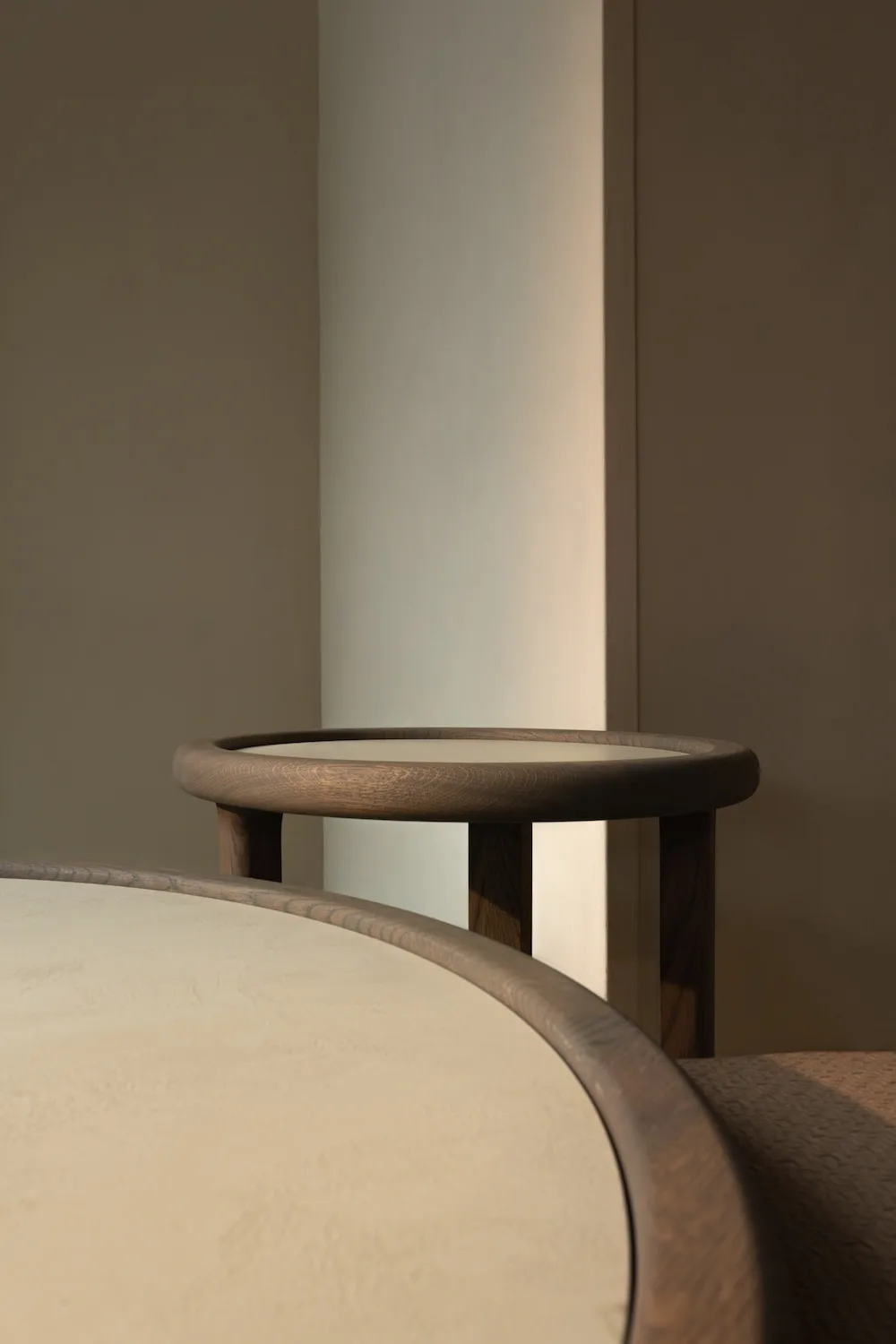 Close-up of two overlapping Amalfi Coffee Tables with softly textured beige tops and rounded dark wooden frames.
