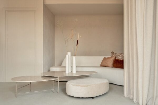 Como Coffee Table Metal set in front of a curved cream sofa with warm-toned cushions, featuring thin metal legs and high-gloss stone tops.