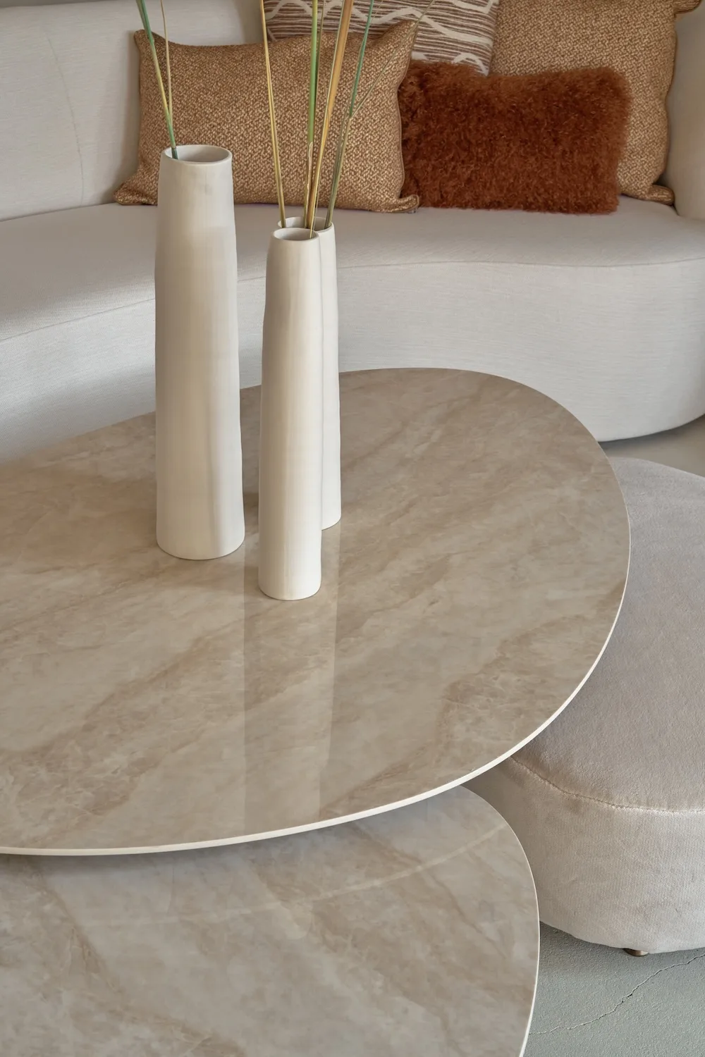 Close-up of glossy Como Coffee Tables with marble-effect tops and white ceramic vases in a neutral-toned setting.