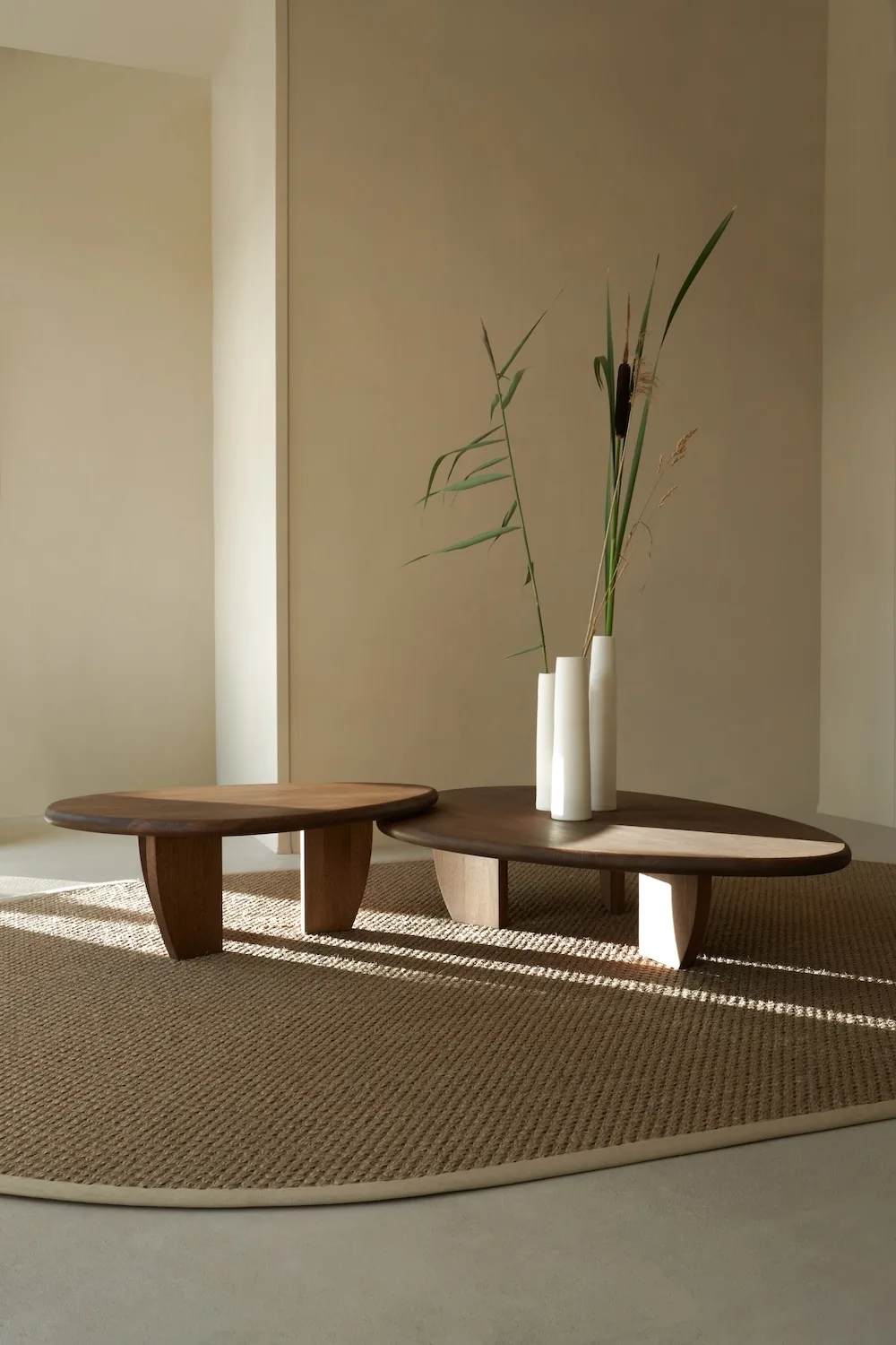 Como Coffee Tables in oak finish styled with tall white vases, set on a round textured rug in a warm, minimalist room.