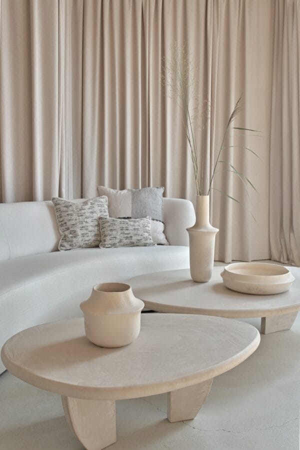 Como Coffee Tables in stucco finish, styled with sculptural ceramics in front of a curved cream sofa with textured cushions.