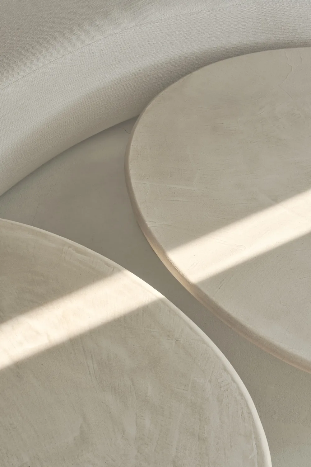 Close-up of two Como Coffee Tables with softly textured stucco tops, partially lit by natural light.