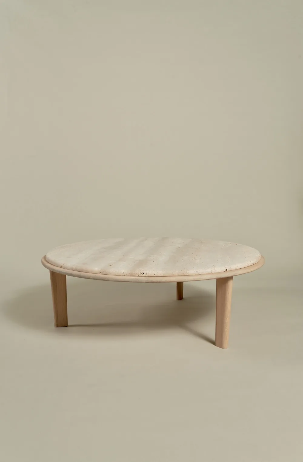 Miller Coffee Table with round travertine top and light wooden legs.
